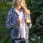 Woman wearing a patterned jacket outdoors with trees in the background