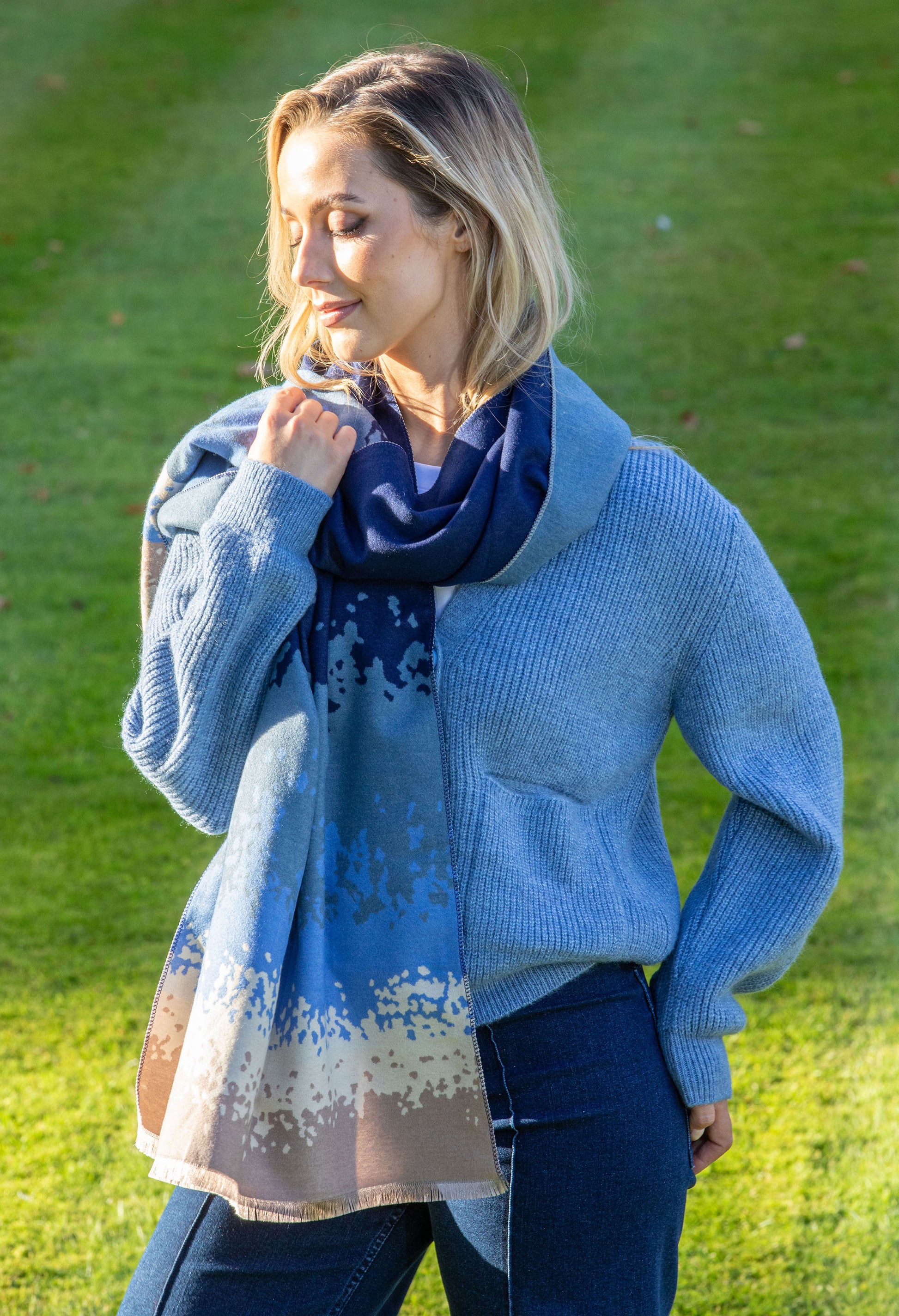 Woman wearing a blue sweater and scarf outdoors on grass