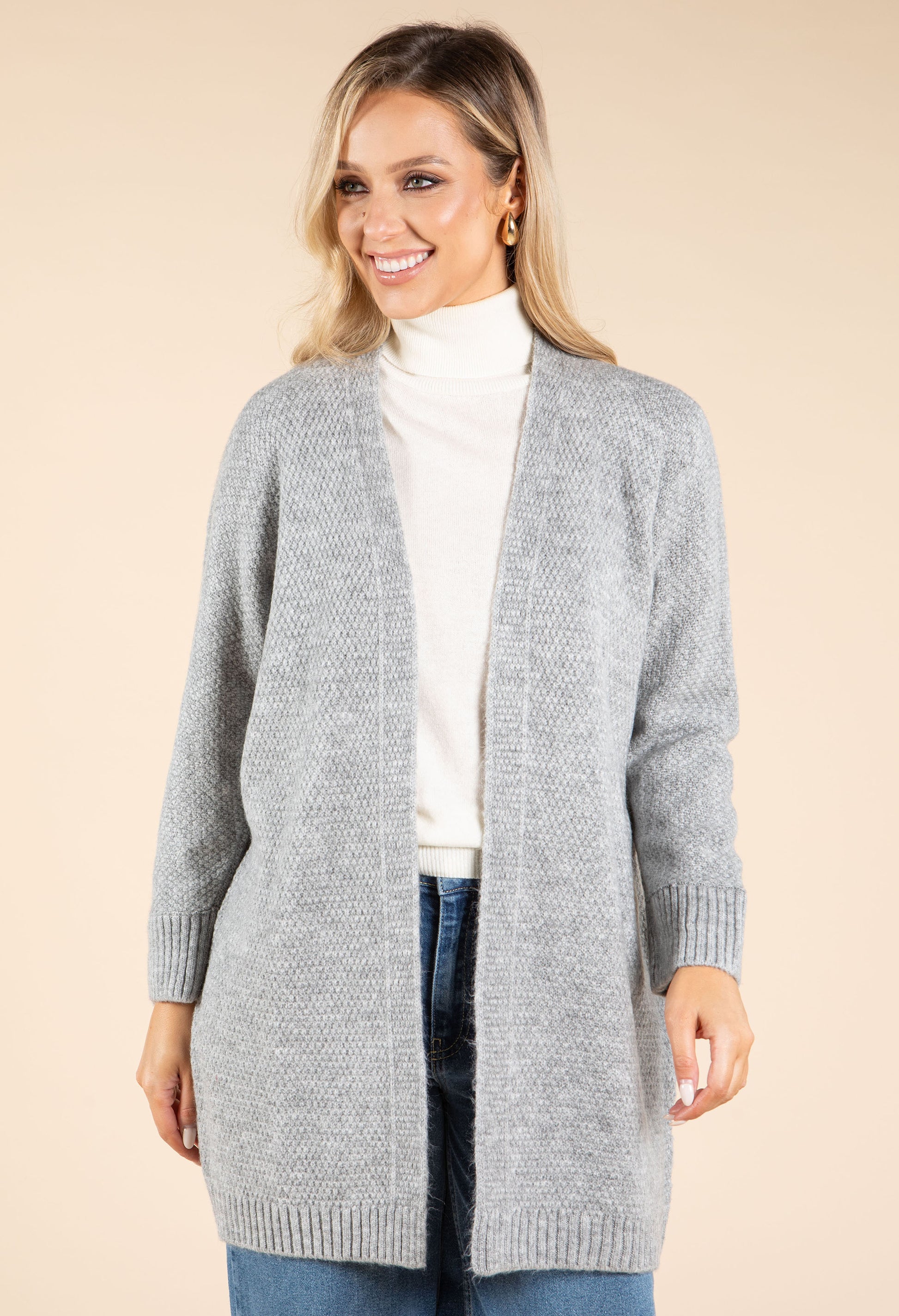 Woman wearing a gray cardigan over a white turtleneck on a beige background