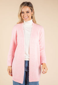 Woman wearing a pink cardigan over a white turtleneck and blue jeans on a beige background