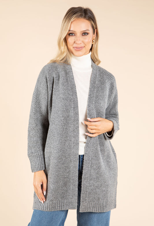 Woman wearing a gray cardigan over a white turtleneck on a beige background