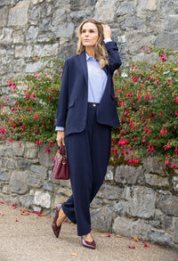 Woman in a navy suit standing in front of a stone wall with red flowers