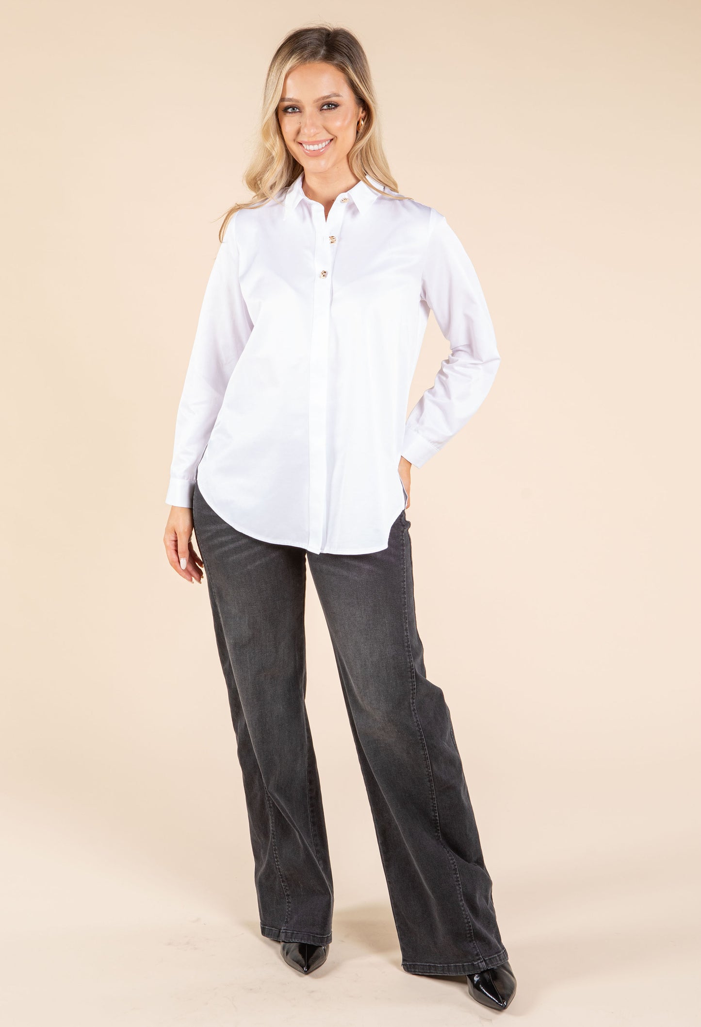 Woman wearing a white shirt and dark jeans on a beige background