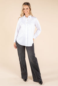 Woman wearing a white shirt and dark jeans on a beige background