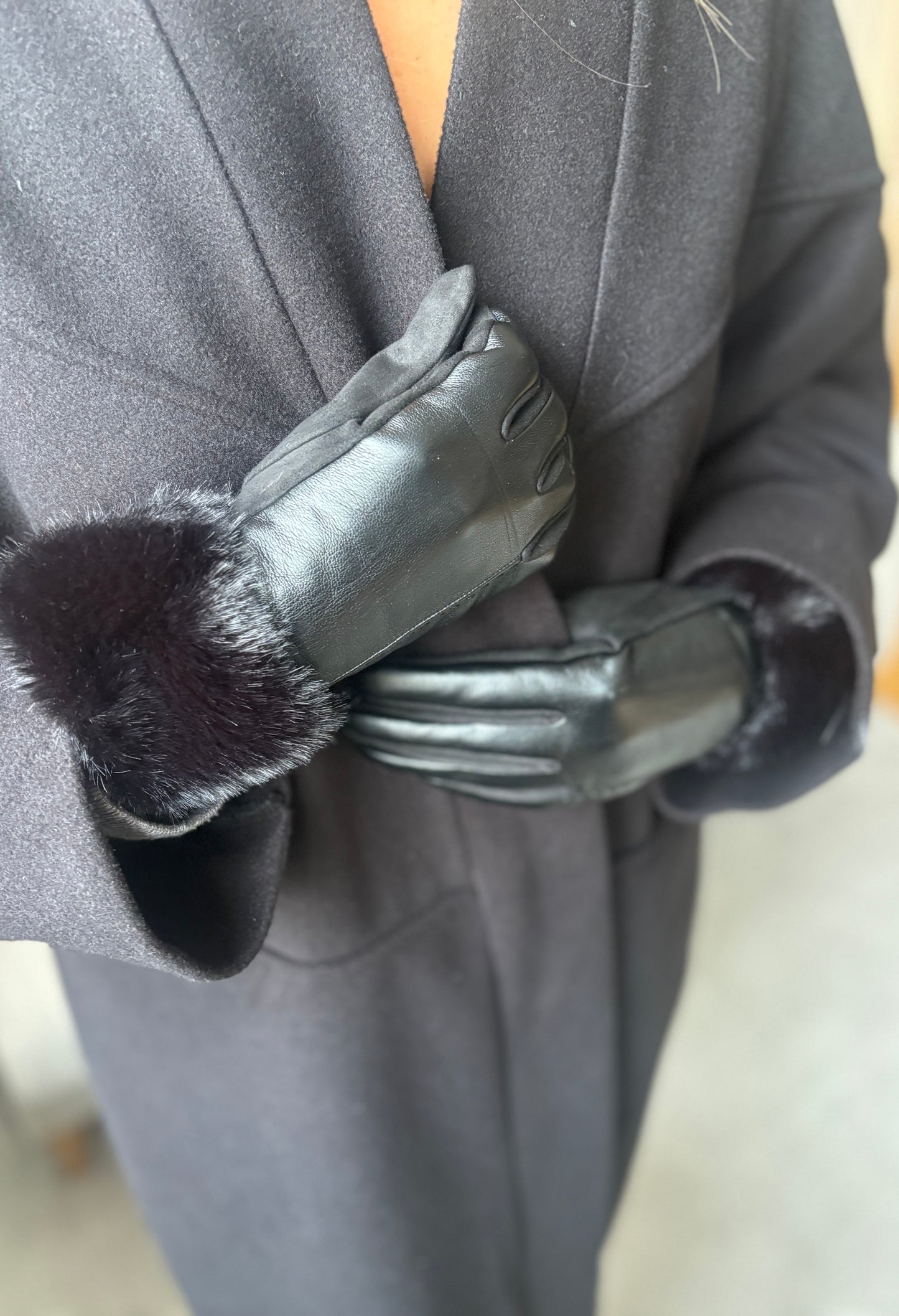 Gray coat with black leather gloves and fur cuffs on a blurred background