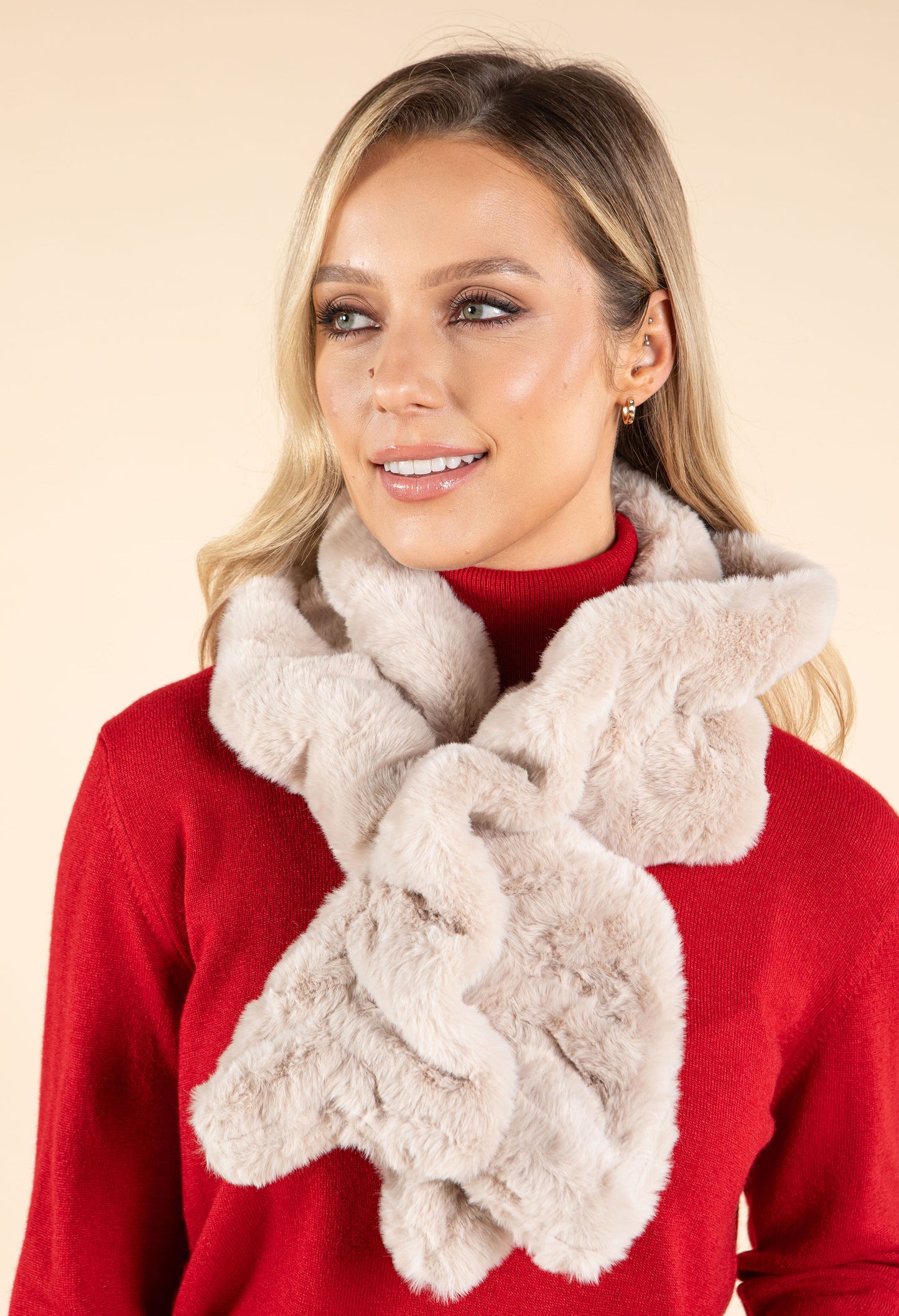Woman wearing a red sweater and beige fluffy scarf against a beige background