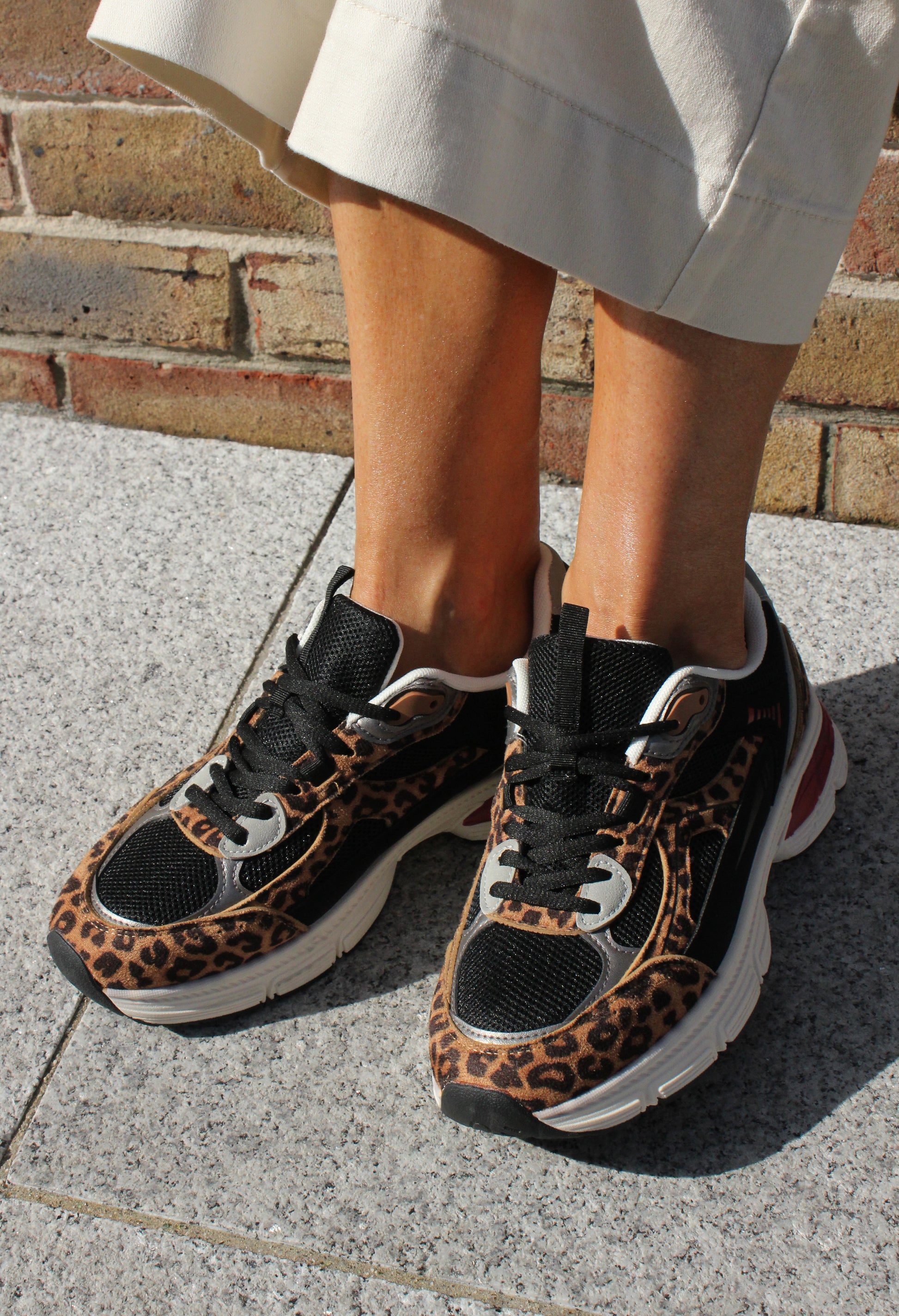 Leopard print sneakers worn on a concrete surface with a brick wall in the background