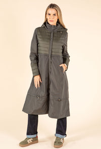 Woman wearing a long, dark green coat with a hood on a beige background