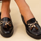 Black loafers with gold accents and leopard print charms on a beige background