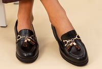 Black loafers with gold accents and leopard print charms on a beige background