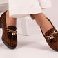 Brown leopard print loafers with gold accents worn by a person sitting on a white chair.