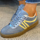 Blue sneakers with yellow accents worn on a textured carpet