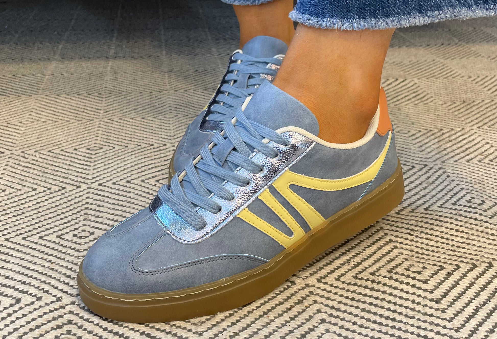 Blue sneakers with yellow accents worn on a textured carpet