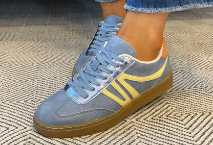 Blue sneakers with yellow accents worn on a textured carpet