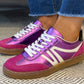 Purple and pink sneakers with white laces worn indoors on a textured floor.