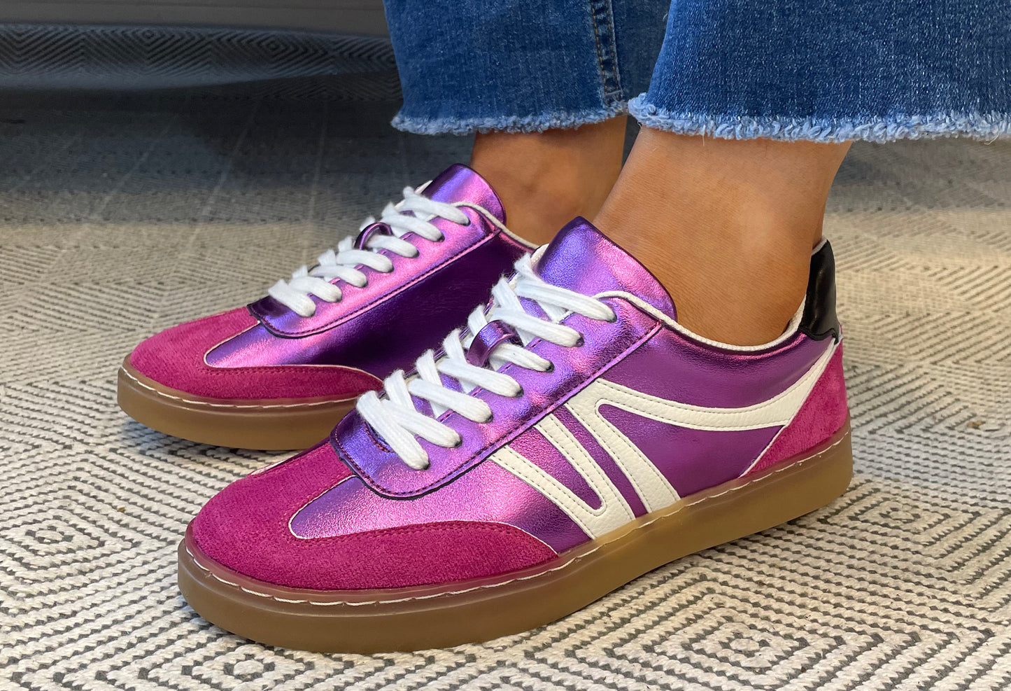 Purple and pink sneakers with white laces worn indoors on a textured floor.