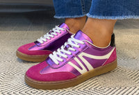 Purple and pink sneakers with white laces worn indoors on a textured floor.