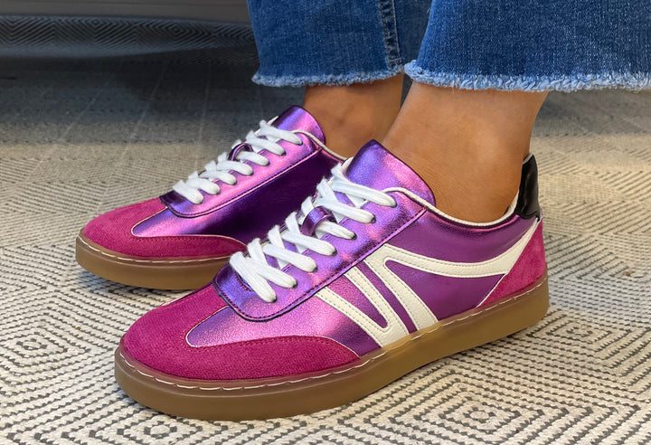 Purple and pink sneakers with white laces worn indoors on a textured floor.