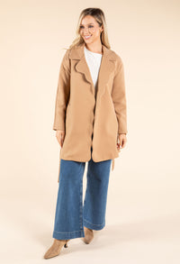 Woman wearing a beige coat and blue jeans on a beige background