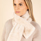 Woman wearing a beige sweater with a white fur-trimmed scarf against a beige background