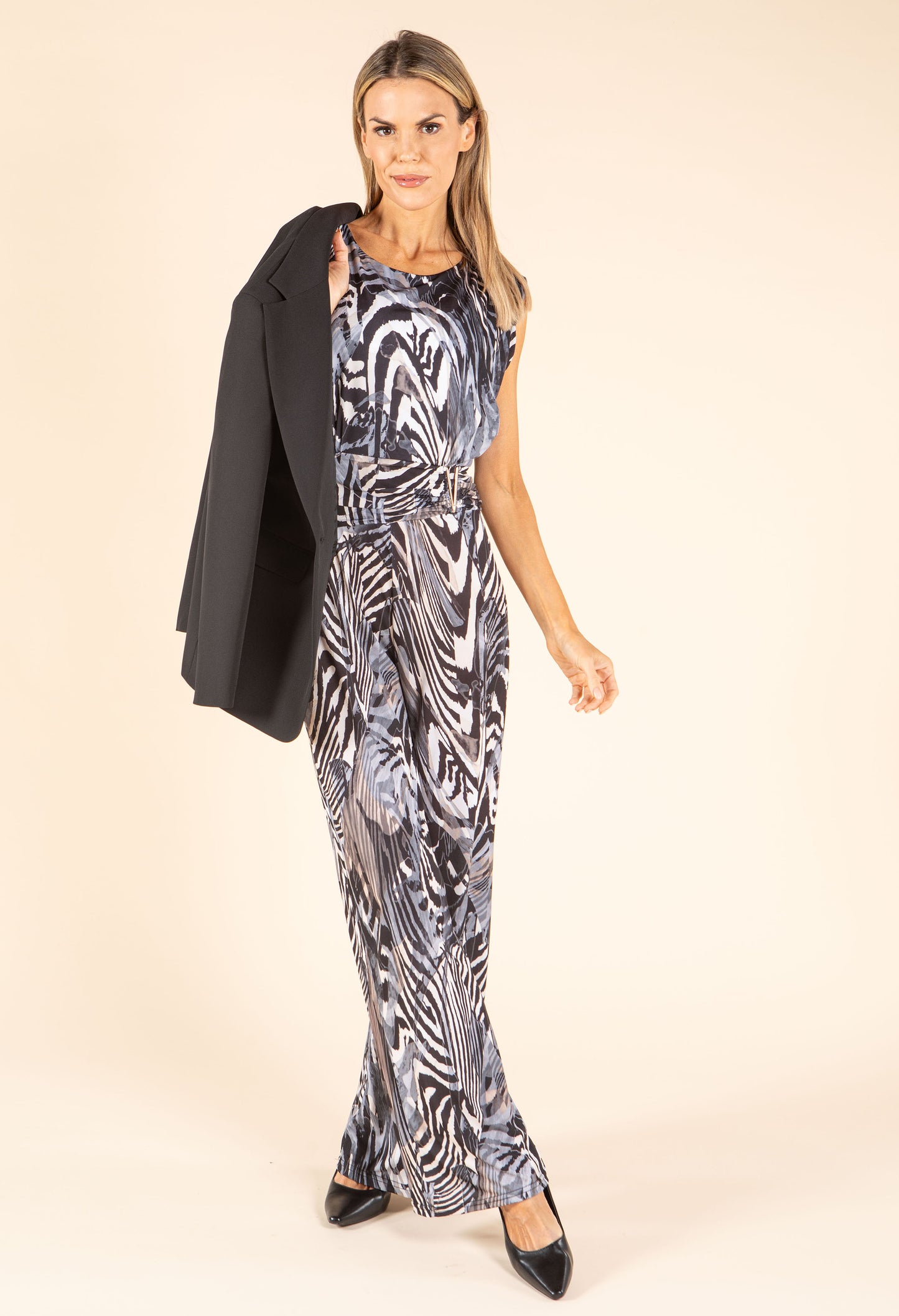 Woman wearing a patterned jumpsuit with a black jacket on a beige background