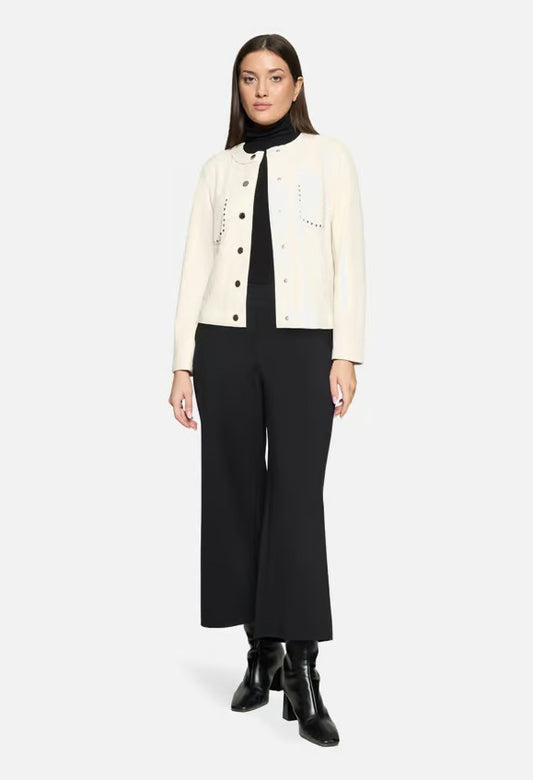 Woman wearing a cream jacket over a black top and pants on a white background