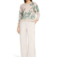 Woman wearing a beige sweater with green leaf pattern and white pants on a white background