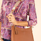 Person wearing a patterned shirt and holding a brown handbag against a beige background