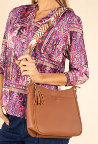 Person wearing a patterned shirt and holding a brown handbag against a beige background