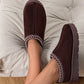 Brown slip-on shoes with white stitching on a light gray cushion.