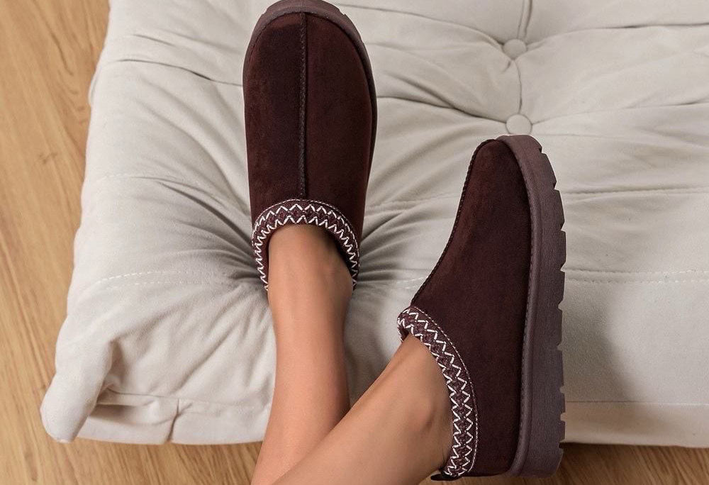 Brown slip-on shoes with white stitching on a light gray cushion.