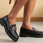Black loafers with gold buckles worn by a person on a neutral background