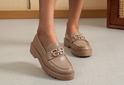 Brown loafers with gold accents worn by a person on a neutral background