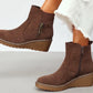 Brown faux suede wedge boot with decorative brass zip on a models foot