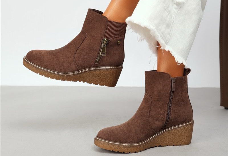 Brown faux suede wedge boot with decorative brass zip on a models foot