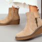 Beige faux suede wedge boot with decorative brass zip on a models foot
