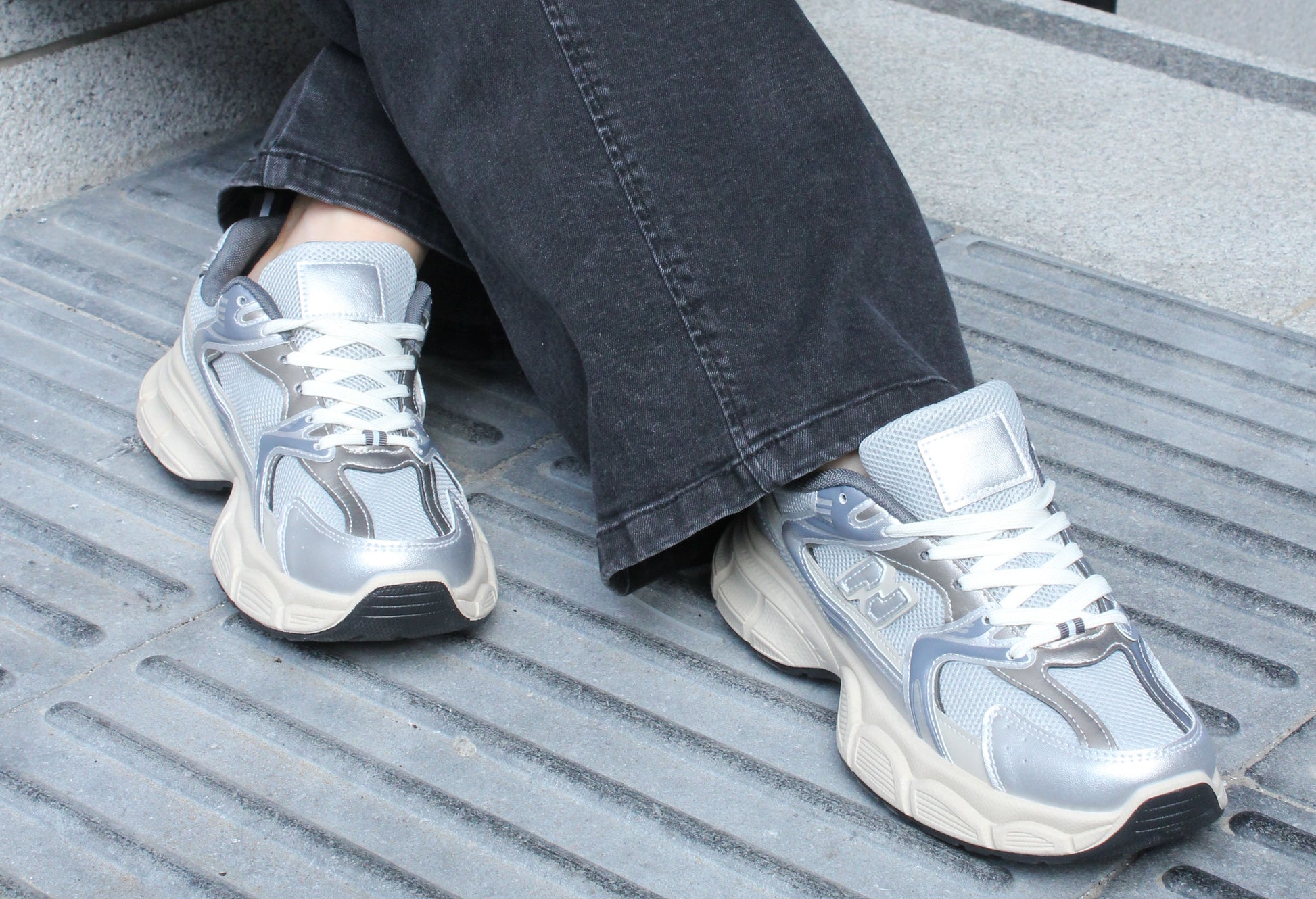 Silver sneakers worn with dark jeans on a textured surface