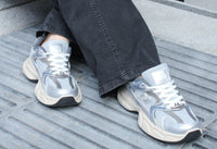 Silver sneakers worn with dark jeans on a textured surface