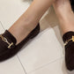 faux suede loafer in brown on a models foot. With a gold buckle detail.