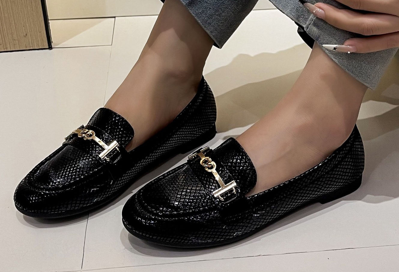 faux snake effect loafer with gold buckle on a models foot with a white background