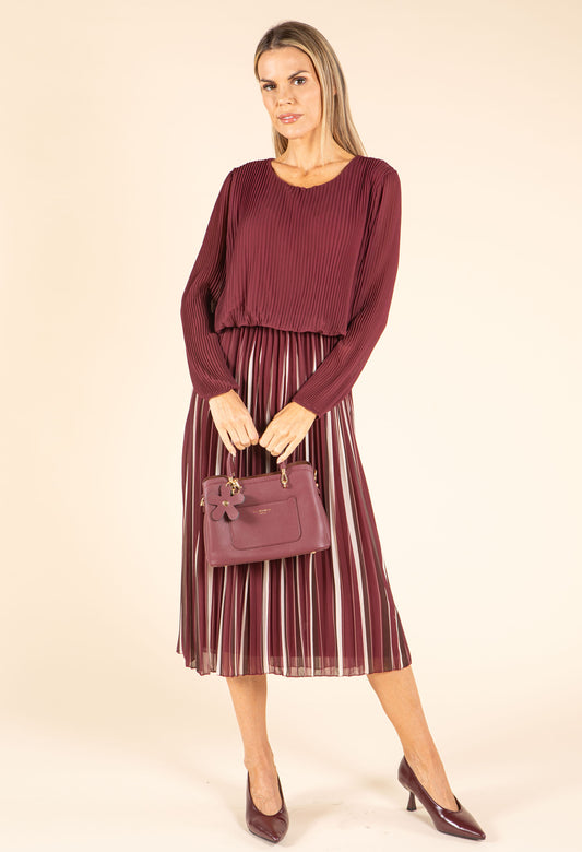 Woman wearing a burgundy top and striped skirt holding a matching handbag on a beige background