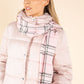 Woman wearing a pink puffer jacket and plaid scarf on a beige background