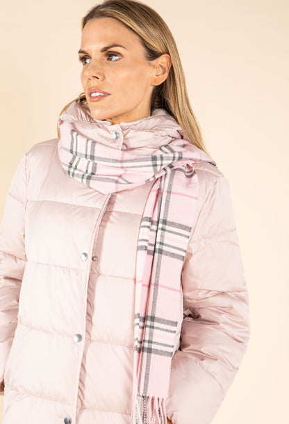 Woman wearing a pink puffer jacket and plaid scarf on a beige background