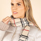 Woman wearing a Burberry scarf and white puffer jacket against a beige background