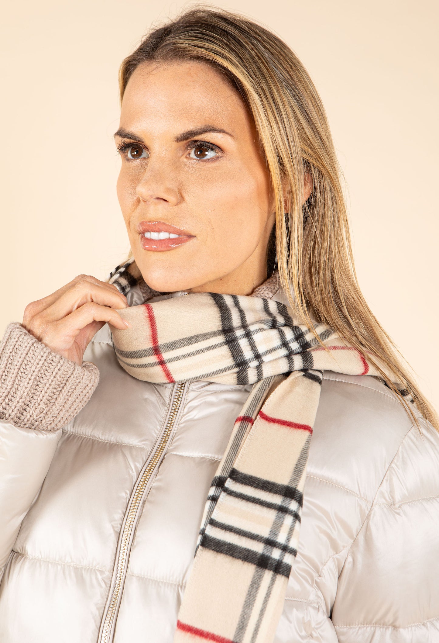 Woman wearing a Burberry scarf and white puffer jacket against a beige background