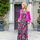 Woman in a floral dress and pink cardigan standing in front of a building with a purple door.