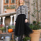 Woman wearing a black and white striped sweater with a black skirt standing outdoors.
