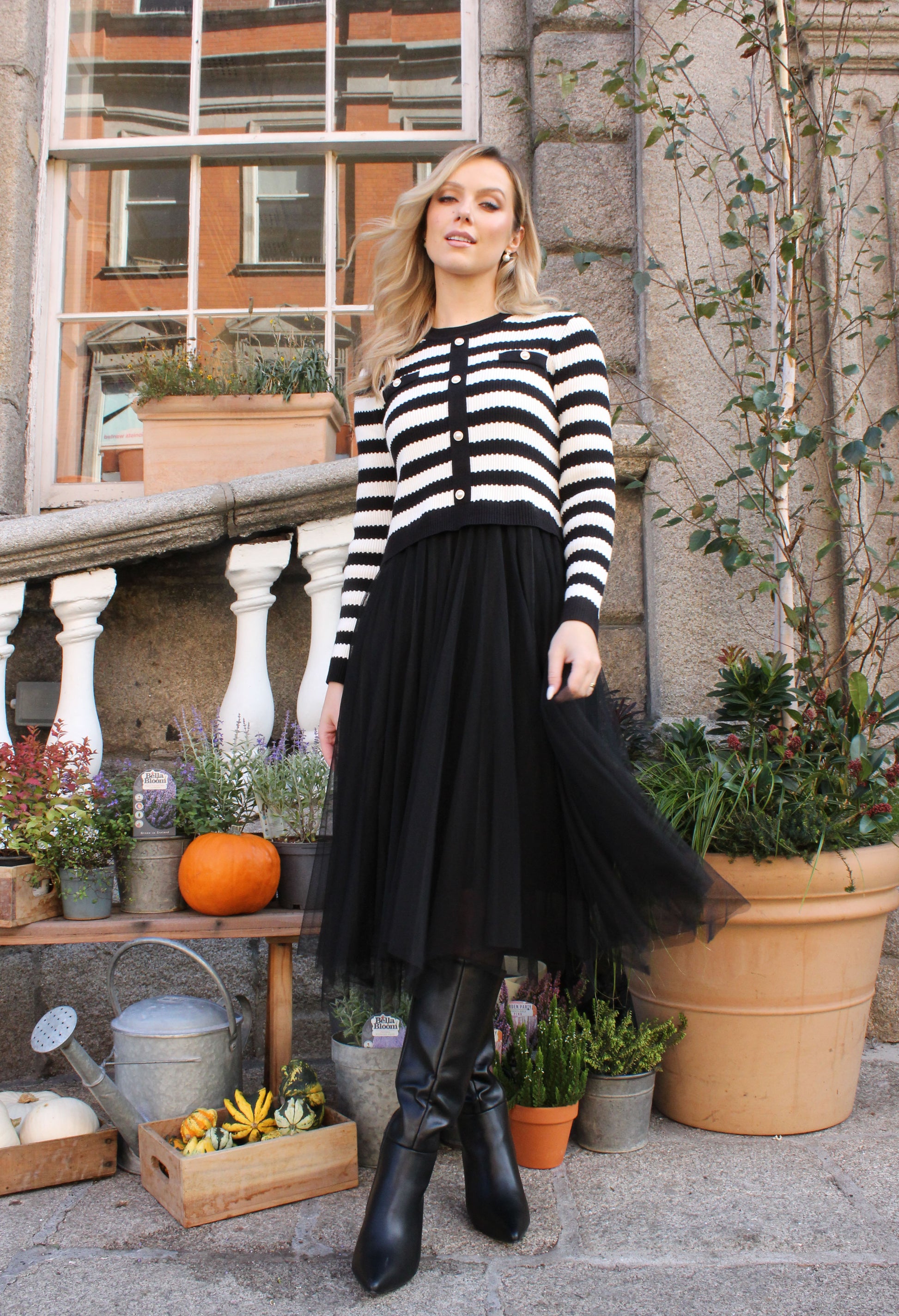 Woman wearing a black and white striped sweater with a black skirt standing outdoors.