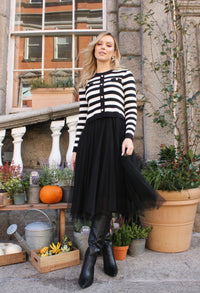 Woman wearing a black and white striped sweater with a black skirt standing outdoors.