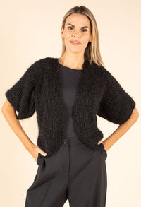 Woman wearing a black textured cardigan over a black top and pants on a beige background